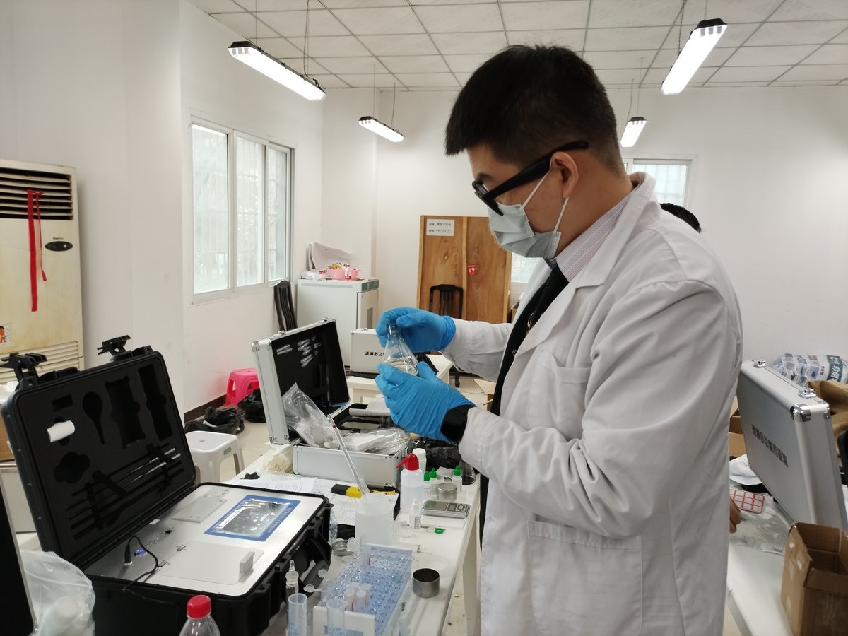 Operator in lab coat and blue gloves preparing a soil extract beside an HM-GT3 analyzer