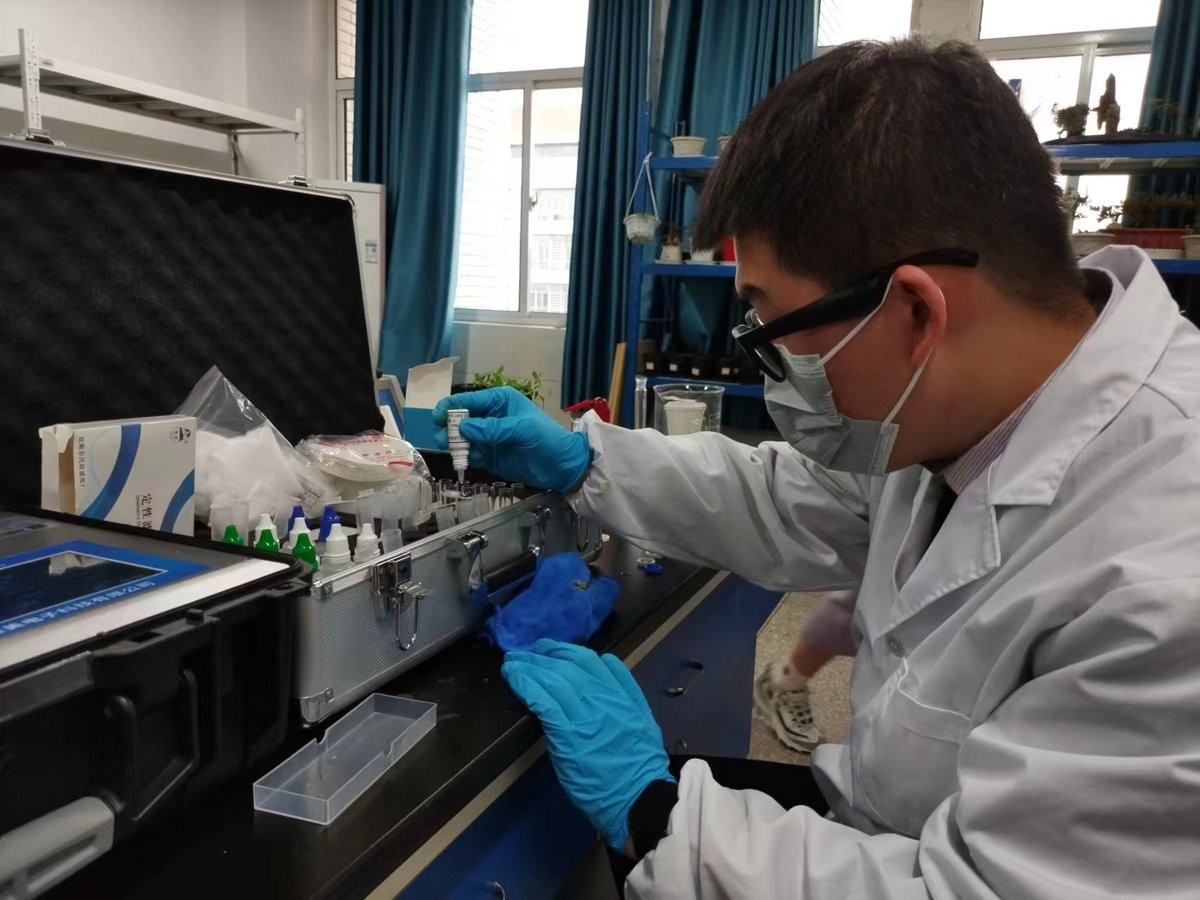 Instructor using dropper to add reagent to test tube during HM-GT4 soil analysis training at Huainan Normal University